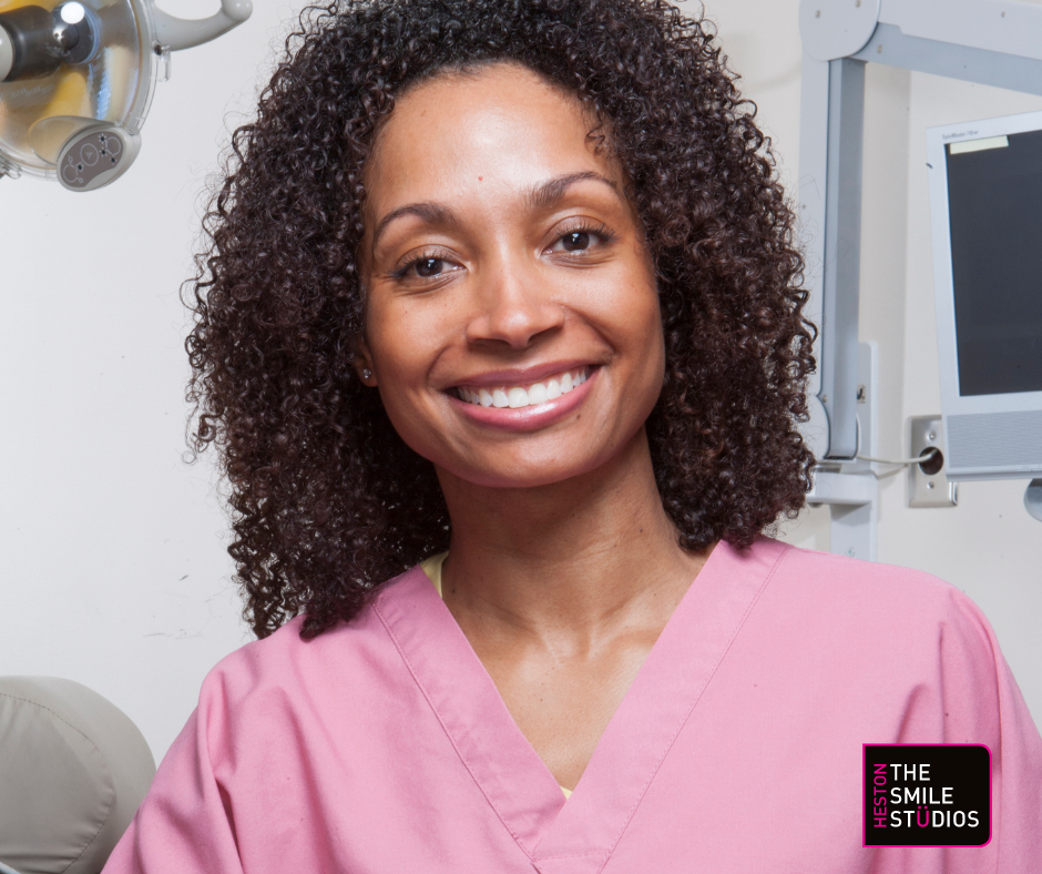 Middle-aged mixed race lady with white teeth wearing a scrub. 