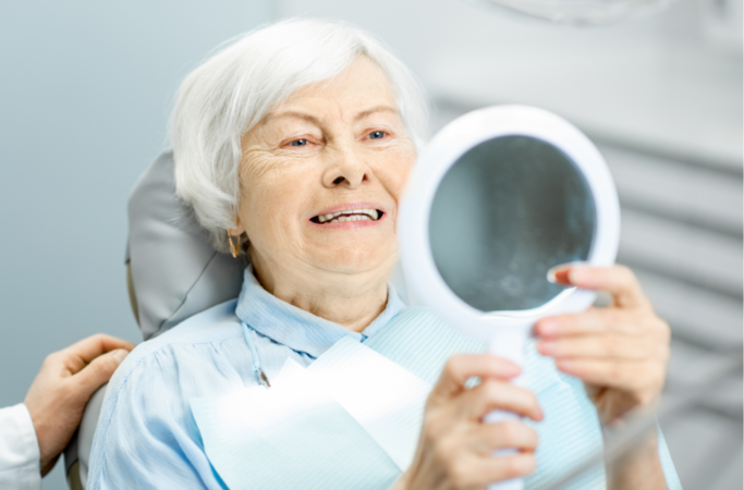 Elderly lady checking her new dentures in the mirror at the dentist.
