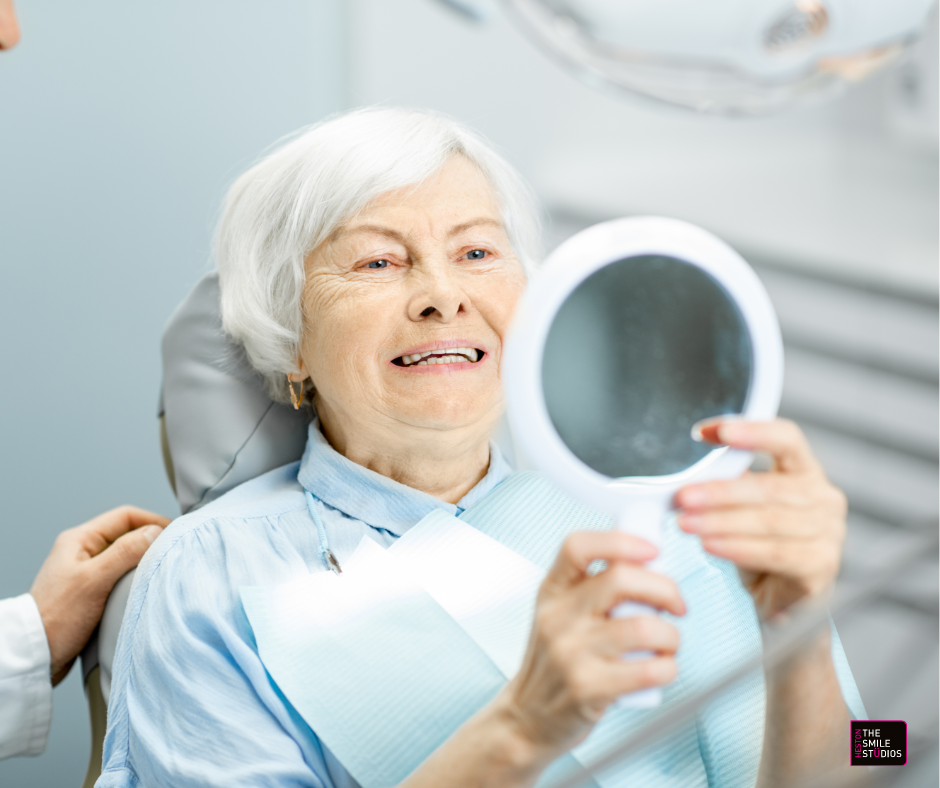 Elderly lady checking her new dentures in the mirror at the dentist. 